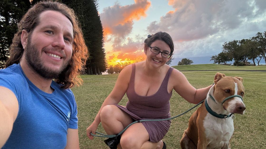 Kevin and Ashley smiling on a fairway at sunset, with Finley on a leash beside Ashley.